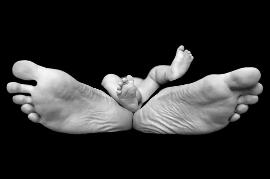 Černobílá fotografie miminka mezi chodidly rodiče