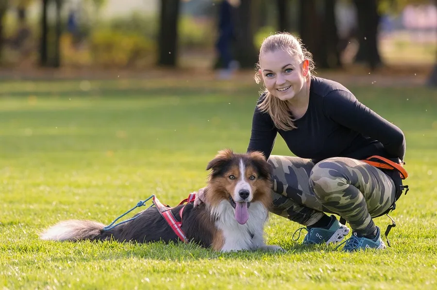 Sportovkyně odpočívající se psem na trávě